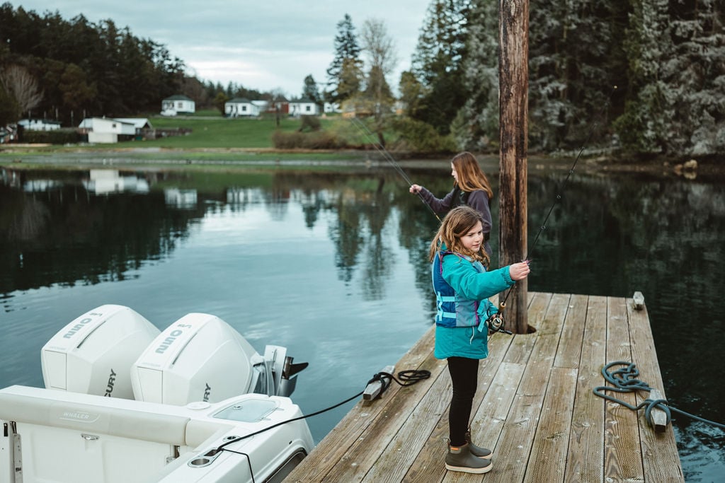 Girls fishing on a dock next a boat with Mercury engines
